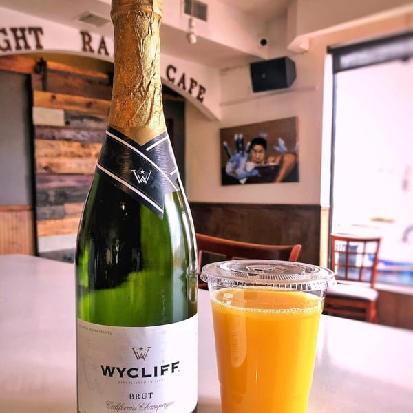 A bottle of Wycliff Brut champagne and a plastic cup of orange juice on a counter at Light Rail Cafe.