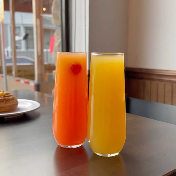 Two tall glasses of juice, one orange with a cherry and one yellow, on a table.
