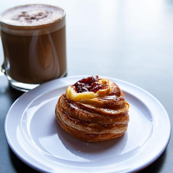 A Light Rail Cafe pastry with jam and a hot chocolate on a white plate.