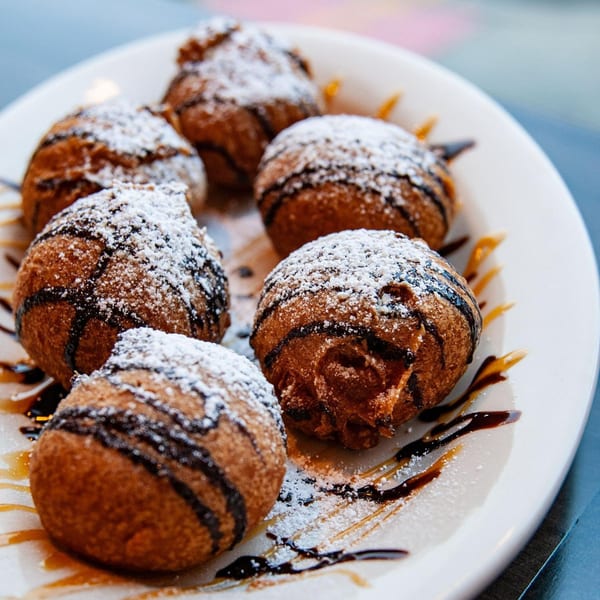 Six deep-fried breakfast pastries, drizzled with chocolate and caramel, dusted with powdered sugar.
