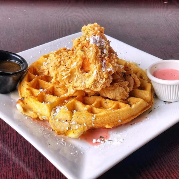 Golden waffle topped with crispy fried chicken, powdered sugar, and two dipping sauces.