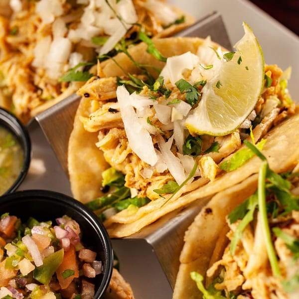 Three chicken tacos with onions, cilantro, and lime, served with salsa and guacamole.