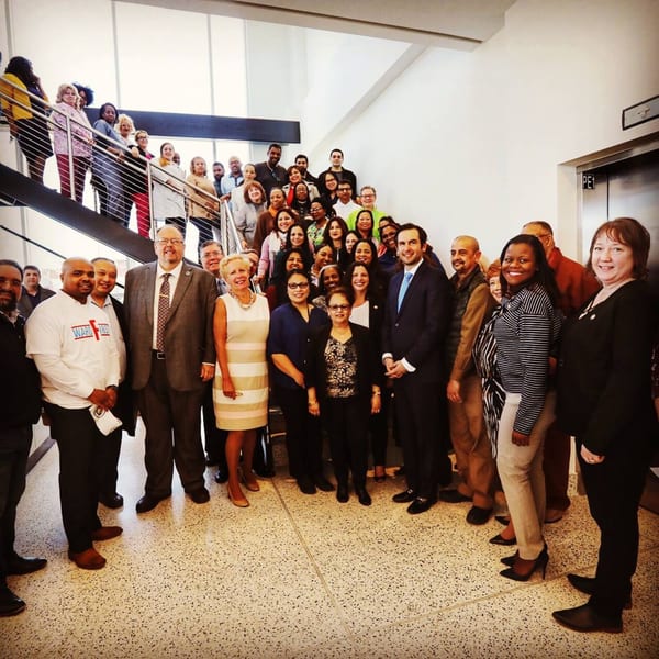 A large group of diverse people, some on stairs and some on the ground floor, smiling at the camera.