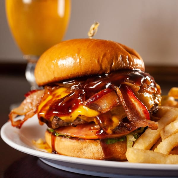 Light Rail Cafe's bacon cheeseburger with BBQ sauce and fries, with a drink in the background.
