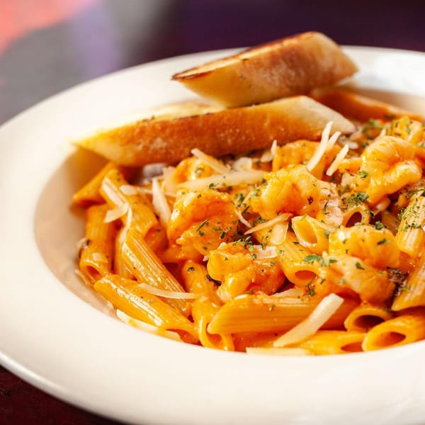 Penne pasta with shrimp in a creamy orange sauce, topped with cheese and parsley, served with bread.