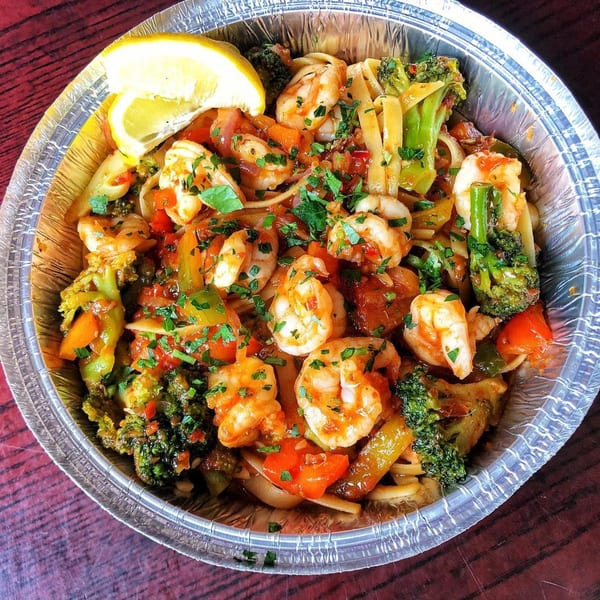 Shrimp and broccoli pasta with red sauce and a lemon wedge in a foil container.